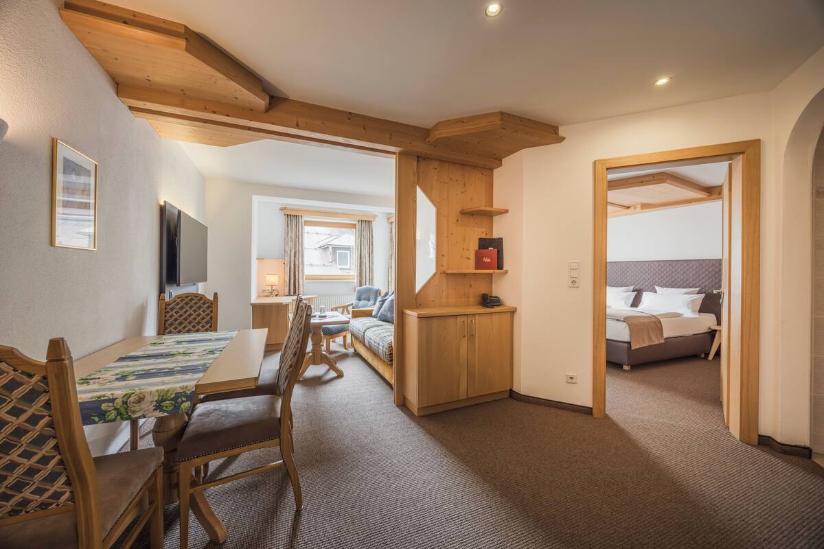 A hotel room with a wooden ceiling, a bed with a grey headboard, a small wooden cabinet, and a TV mounted on the wall.
