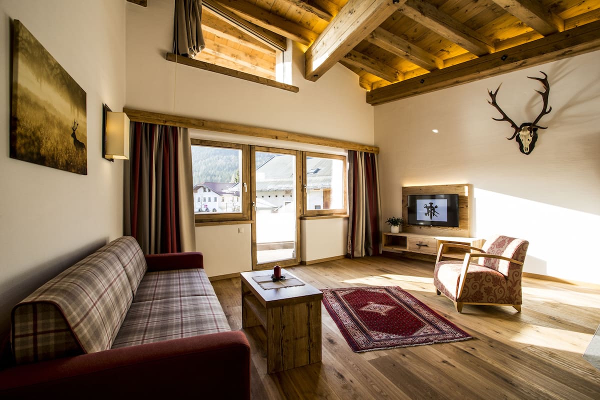 A cozy living room with a sofa, armchair, wooden coffee table, and a mounted deer skull on the wall.