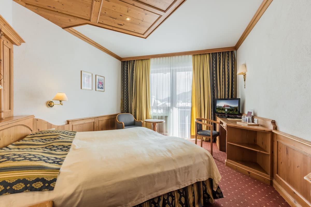 A hotel room with a bed, a desk with a television, a chair, and a small table.