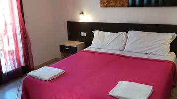 A hotel room with a large bed, a nightstand, a wall-mounted light, and a painting above the bed.
