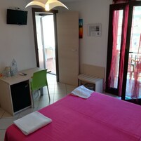 Una habitación de hotel con cama, escritorio, silla, televisión y ventana con cortinas.