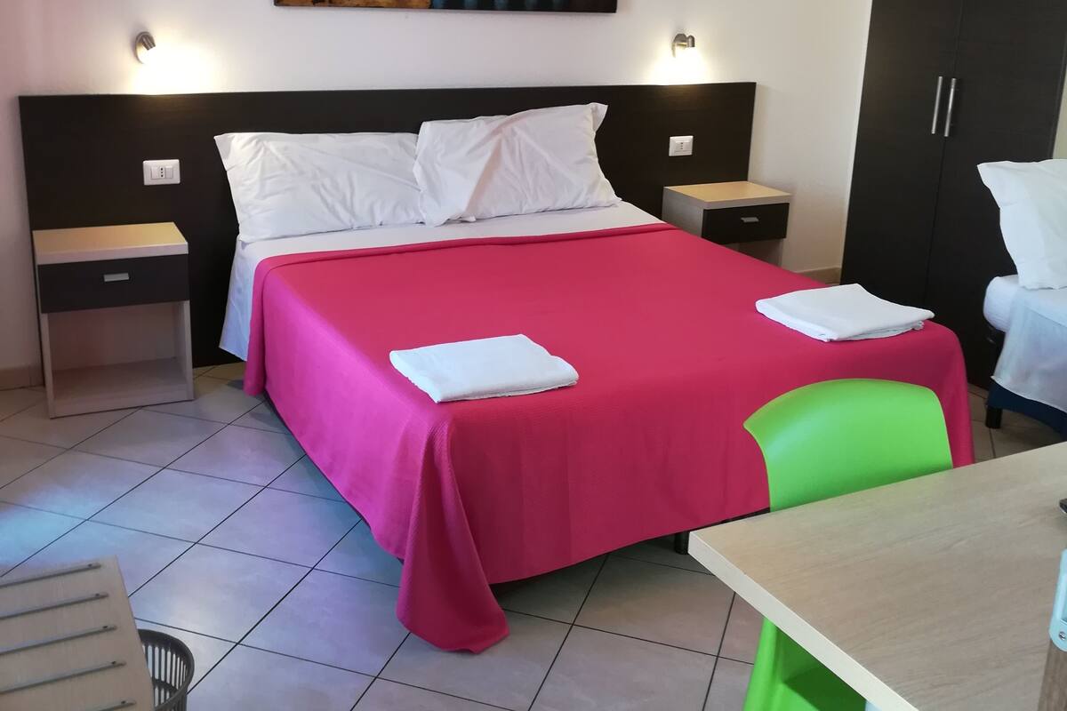A hotel room with a large bed, a desk, a chair, and a wardrobe.