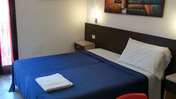 A hotel room with a large bed, a nightstand, a desk, and a chair. There is a painting on the wall and a window with curtains.