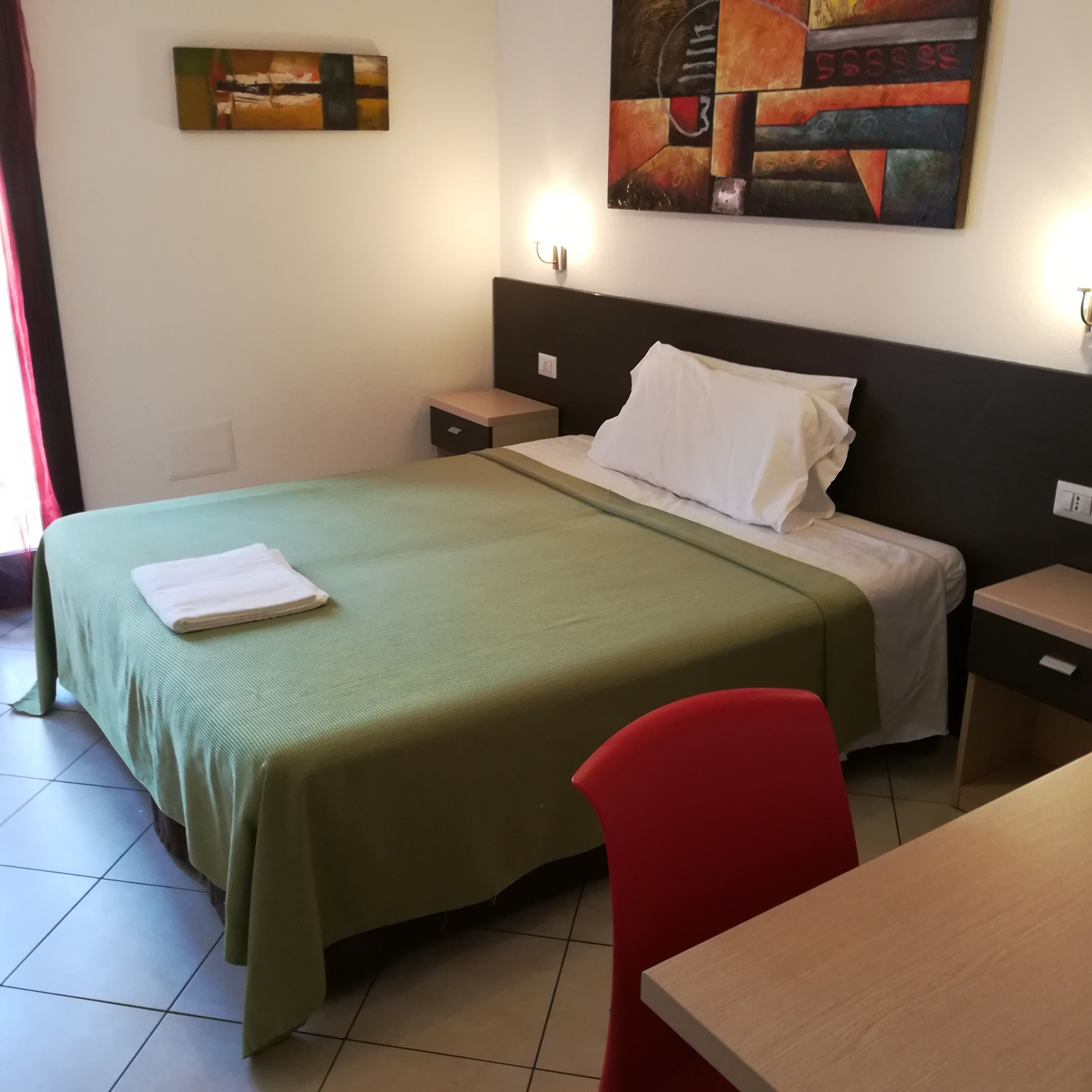 A hotel room with a bed, a nightstand, a desk, and a chair.