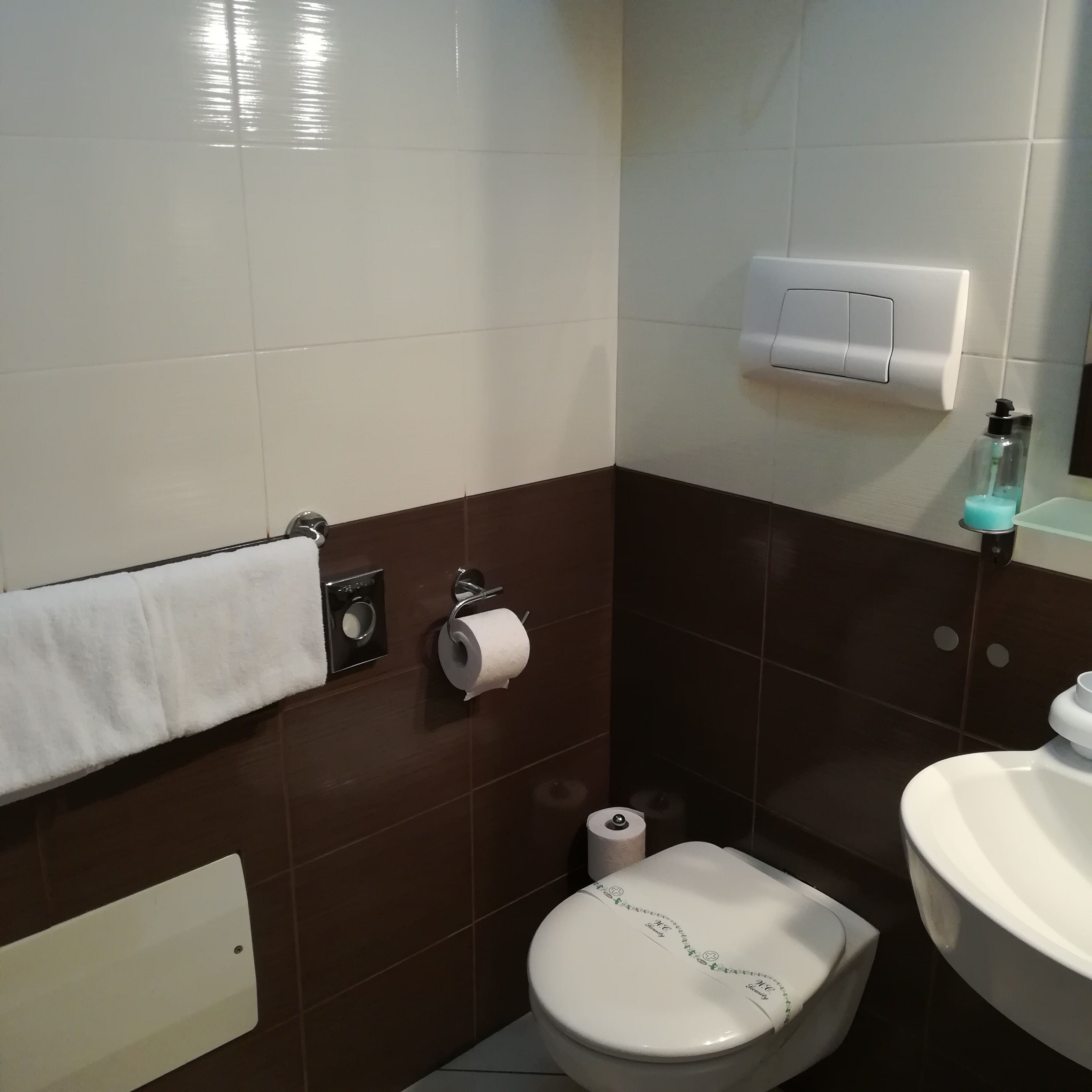 Une salle de bain avec des toilettes blanches, un porte-serviettes avec une serviette blanche, un distributeur d’essuie-tout et un distributeur de savon.