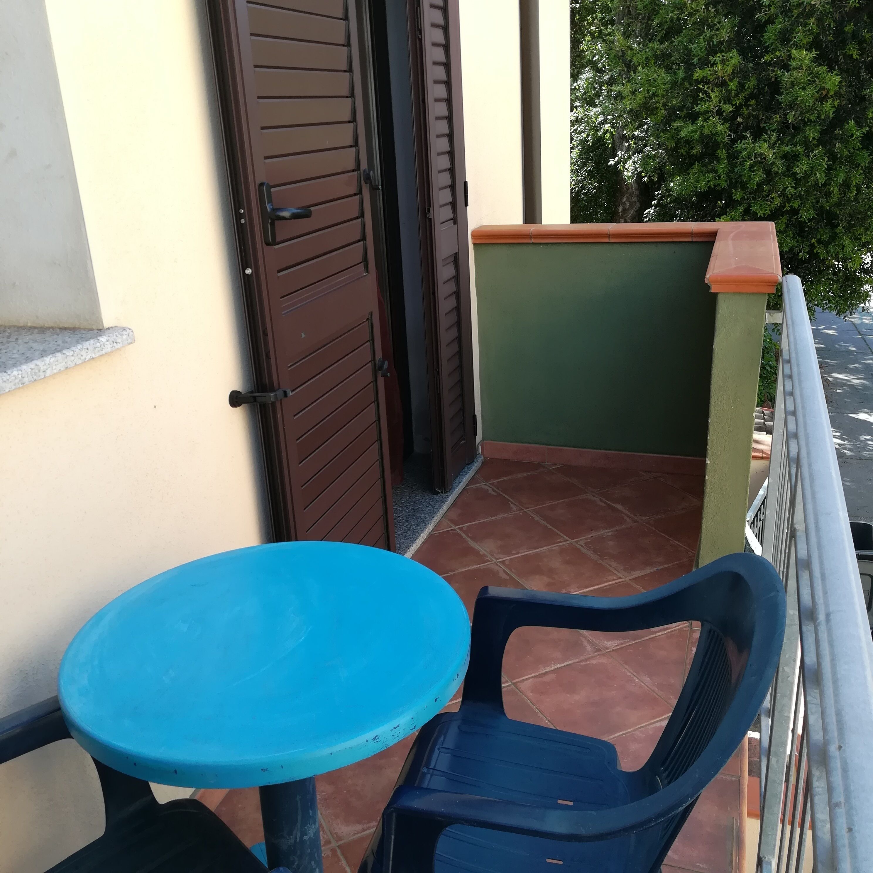 Een klein balkon met een blauwe tafel en een blauwe stoel, een bruine deur en een groene muur.