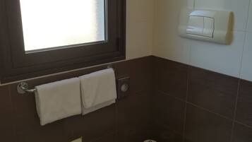A small bathroom with a toilet, a towel rack with two towels, a window, and a paper towel dispenser.