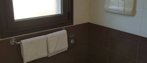 A small bathroom with a toilet, a towel rack with two towels, a window, and a paper towel dispenser.