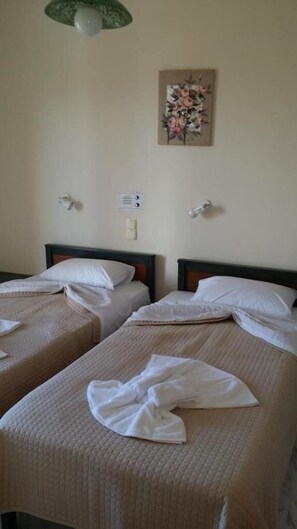 Two single beds with white linens, a wall-mounted light fixture, a power outlet, and a floral artwork on the wall. - Mythos Beach Hotel (Platanias)