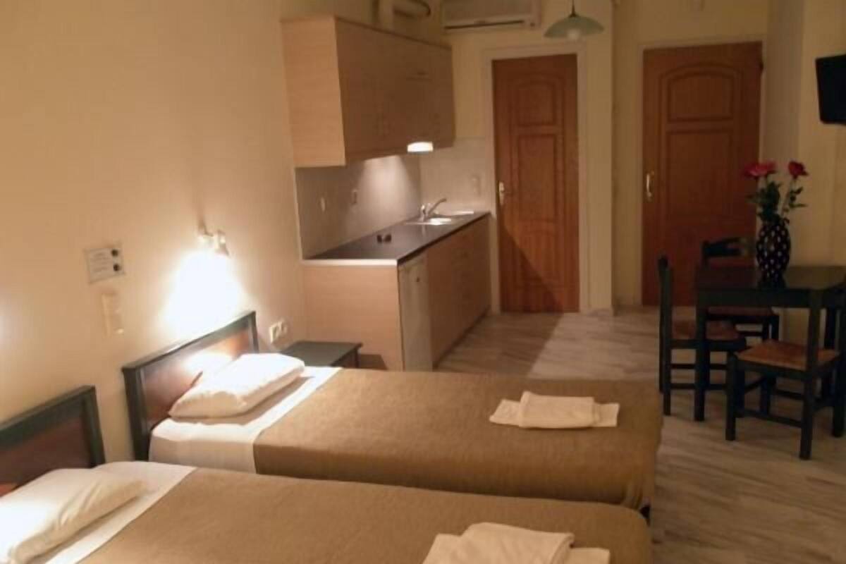 A hotel room with two beds, a small kitchenette, a dining table with chairs, and a wooden door.