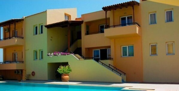 A multi-story hotel with balconies, a swimming pool, and a staircase leading to the upper floors. - Mythos Beach Hotel (Platanias)