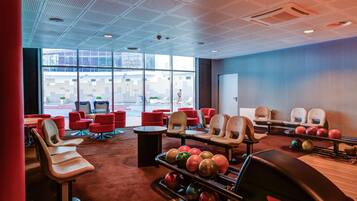 A bowling alley with multiple lanes, red and beige chairs, and a large window providing a view of the outside.