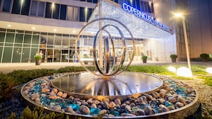 A hotel entrance with a modern sign, a circular water feature, and a well-maintained garden.