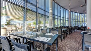A modern restaurant with large windows, tables set with menus, and a patterned carpet.