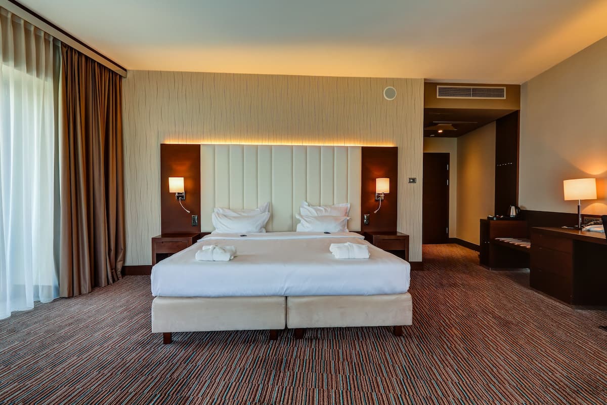 Quarto de hotel com uma cama grande, duas mesas de cabeceira, uma escrivaninha e uma cadeira.