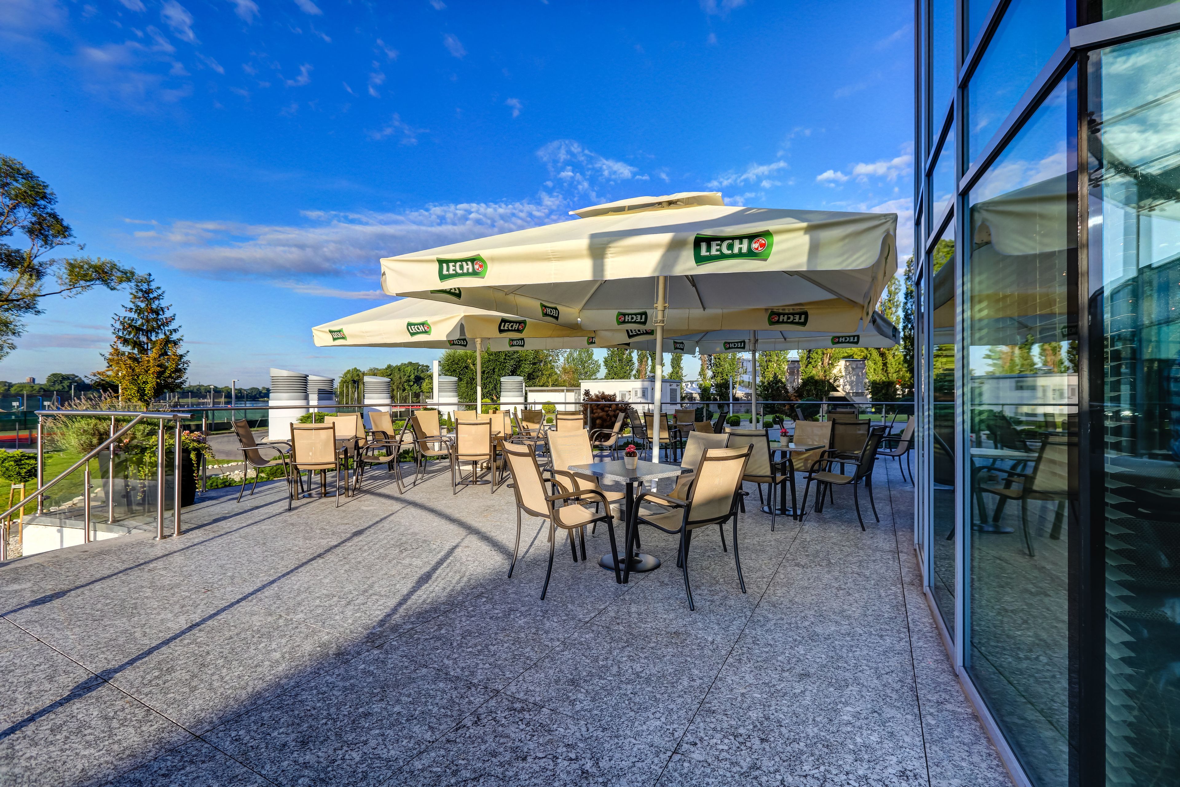 An outdoor patio with tables and chairs, covered by umbrellas, and a glass building in the background.