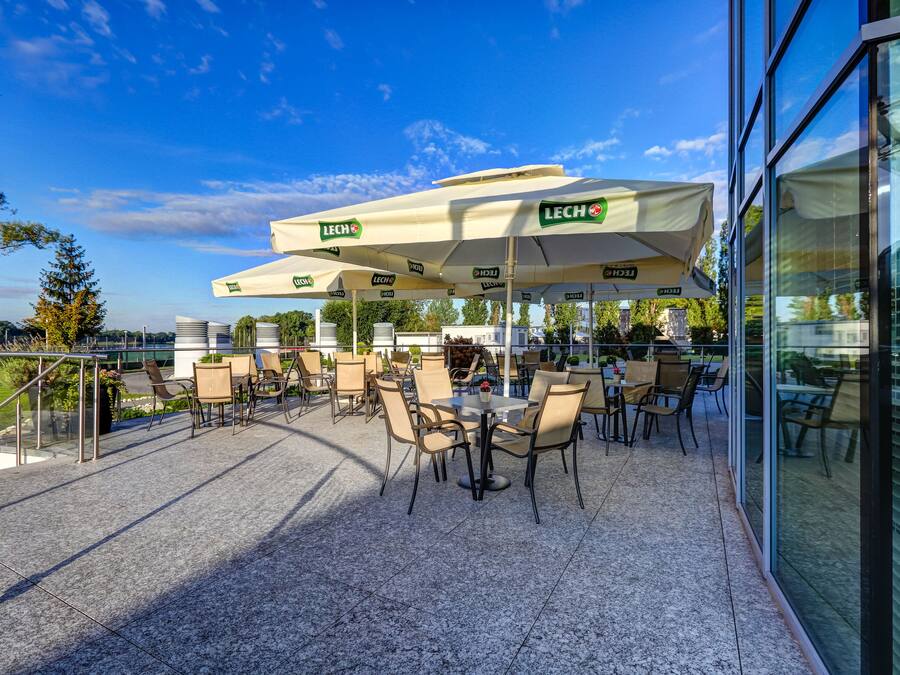 An outdoor patio with tables and chairs, covered by umbrellas, and a glass building in the background.