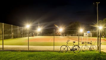 A baseball field at night with floodlights, a bicycle, and a fence.