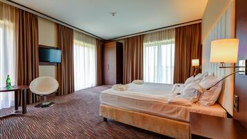 A hotel room with a bed, a desk, a chair, a TV, and a lamp.