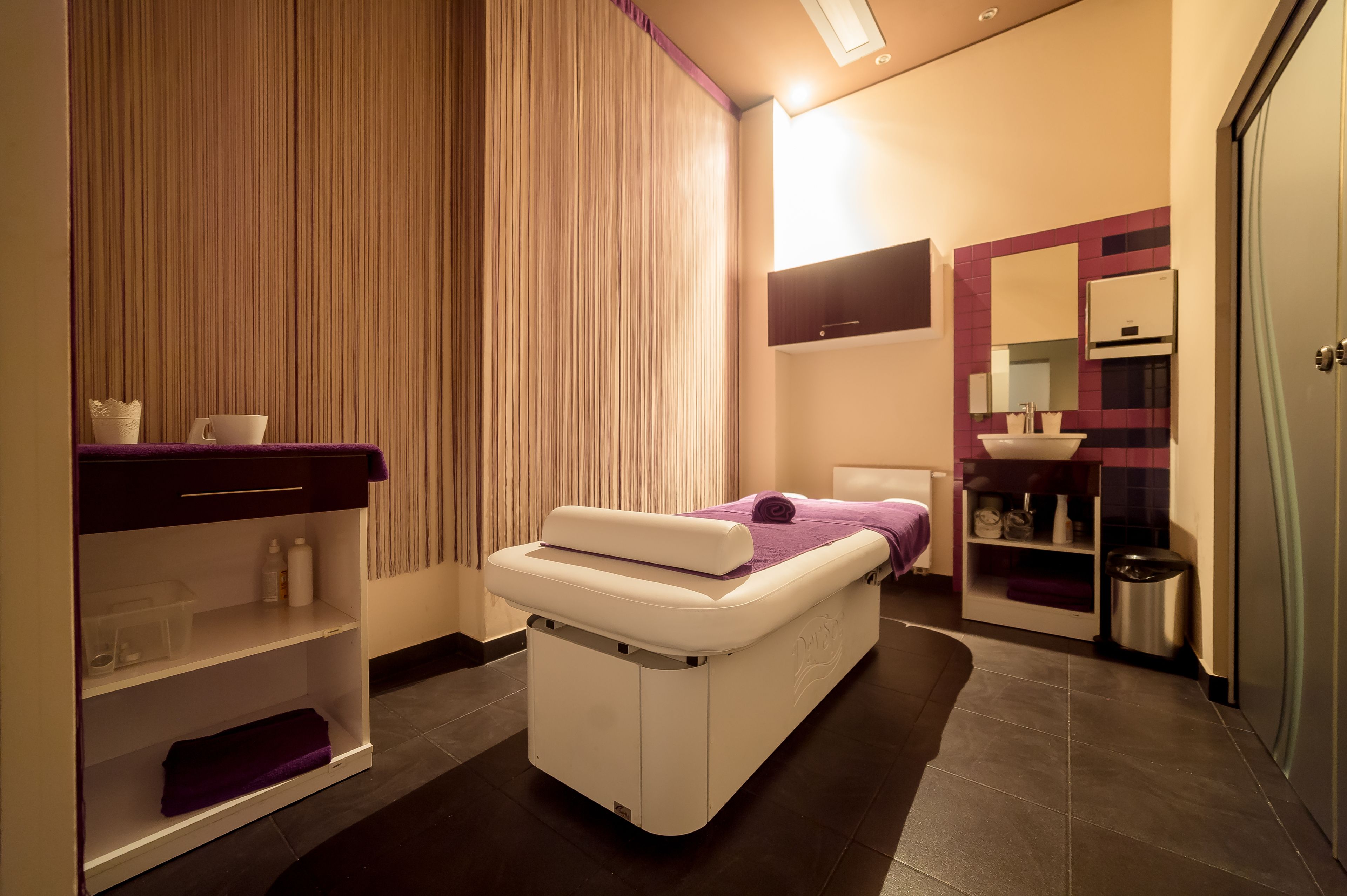 A modern bedroom with a massage table, a vanity with a mirror, and a small kitchenette.