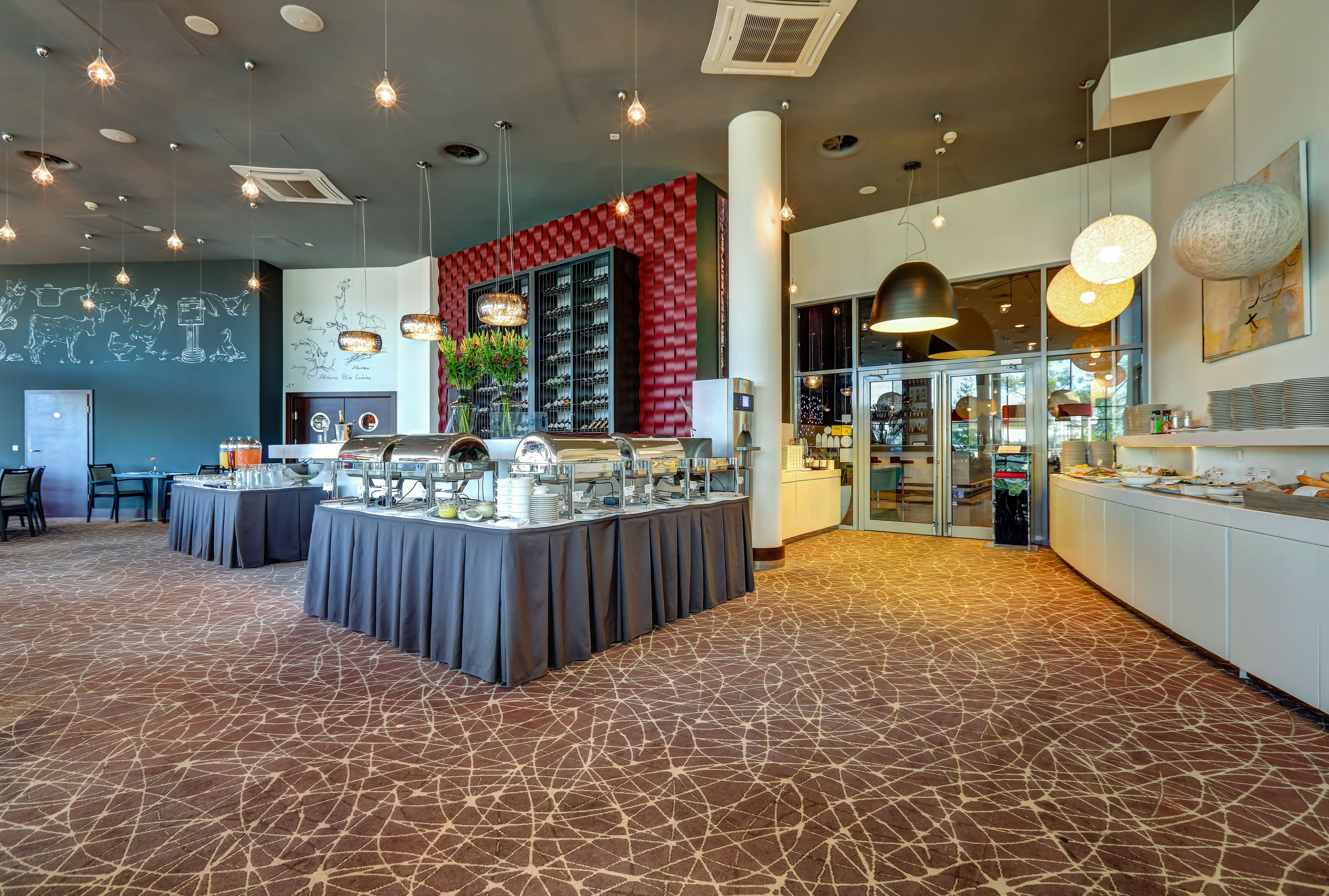 A modern restaurant with a central bar area, a red accent wall, and a patterned carpet.