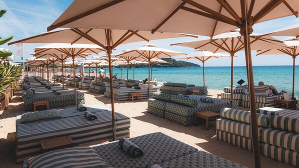 Ein Strandloungebereich mit gestreiften Sofas und Sonnenschirmen mit Blick auf das Meer.
