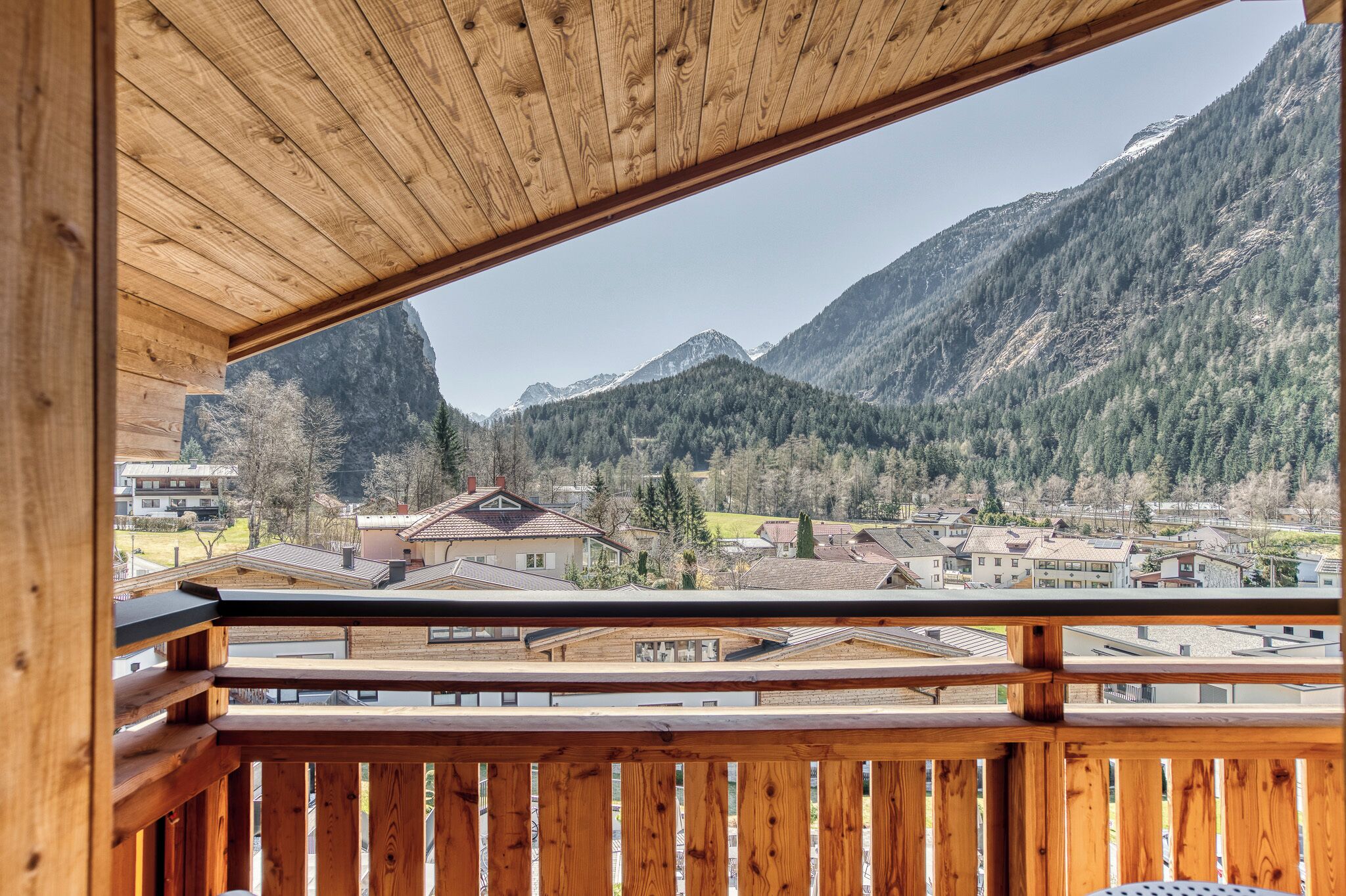 A wooden balcony with a view of a mountainous landscape and residential buildings.