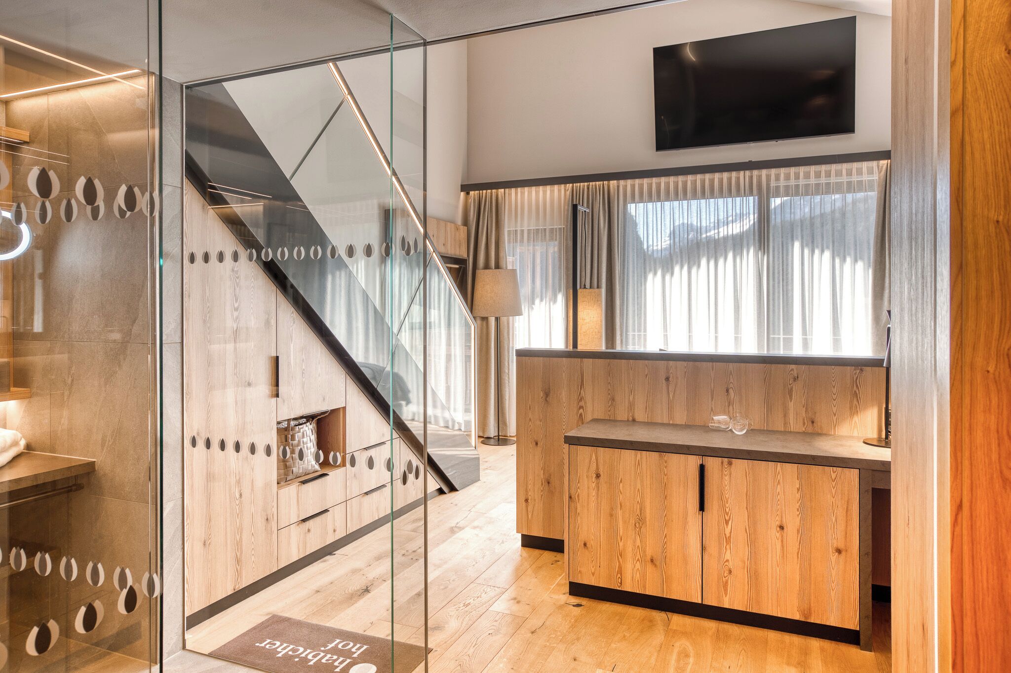 A modern interior with a wooden reception desk, a glass partition, and a staircase.