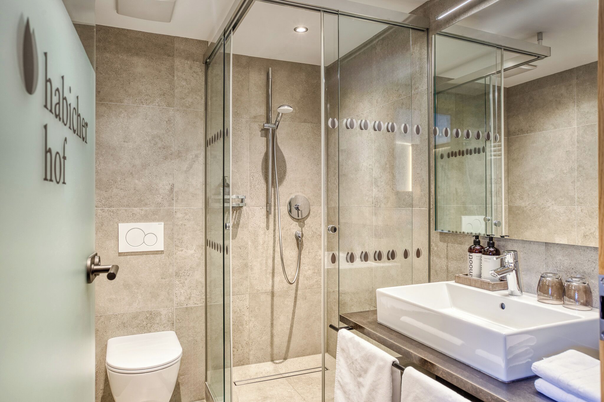 A modern bathroom with a glass-enclosed shower, a white sink, and a mirror.