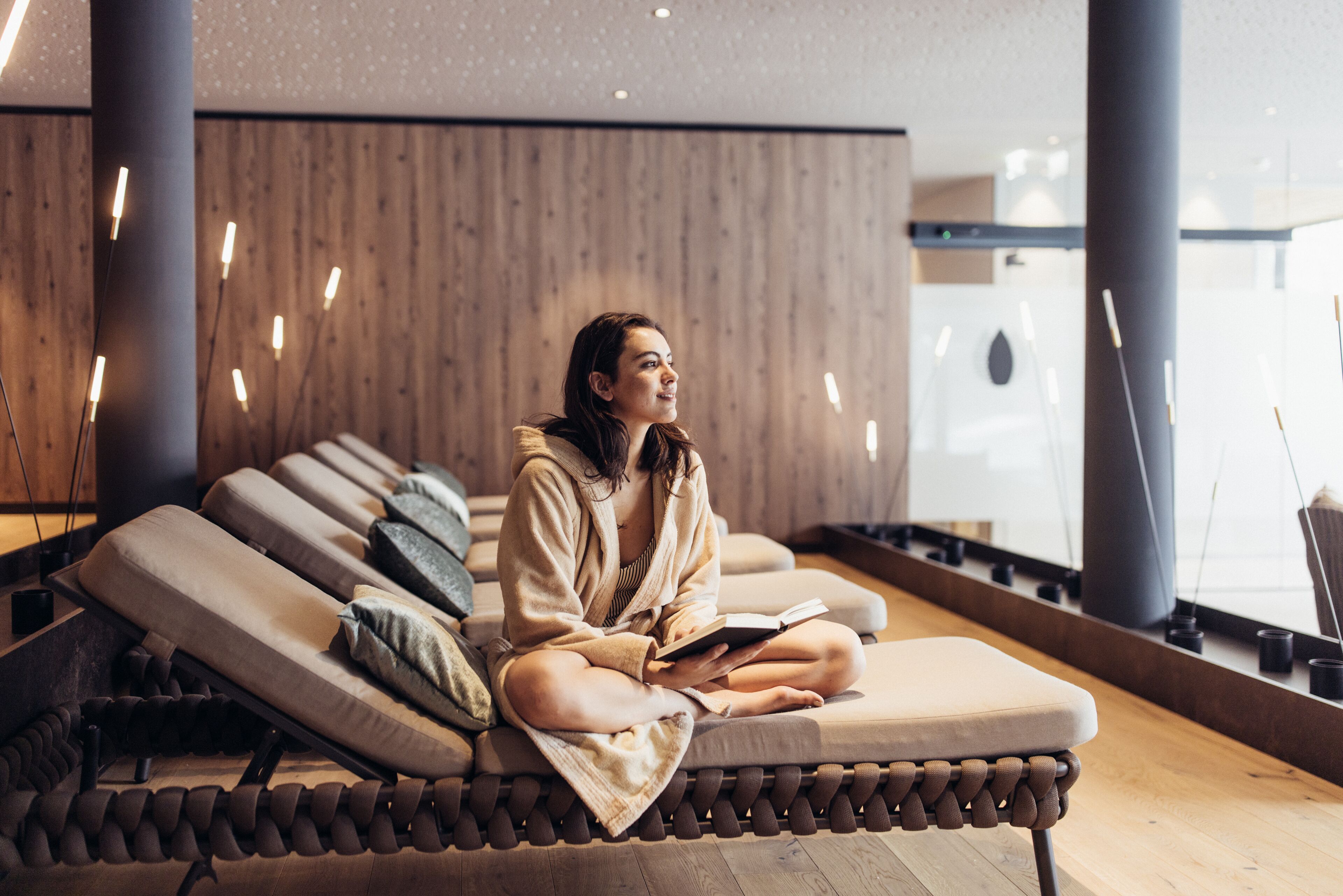 A person sitting on a lounge chair in a modern spa area with wooden paneling and pendant lighting.