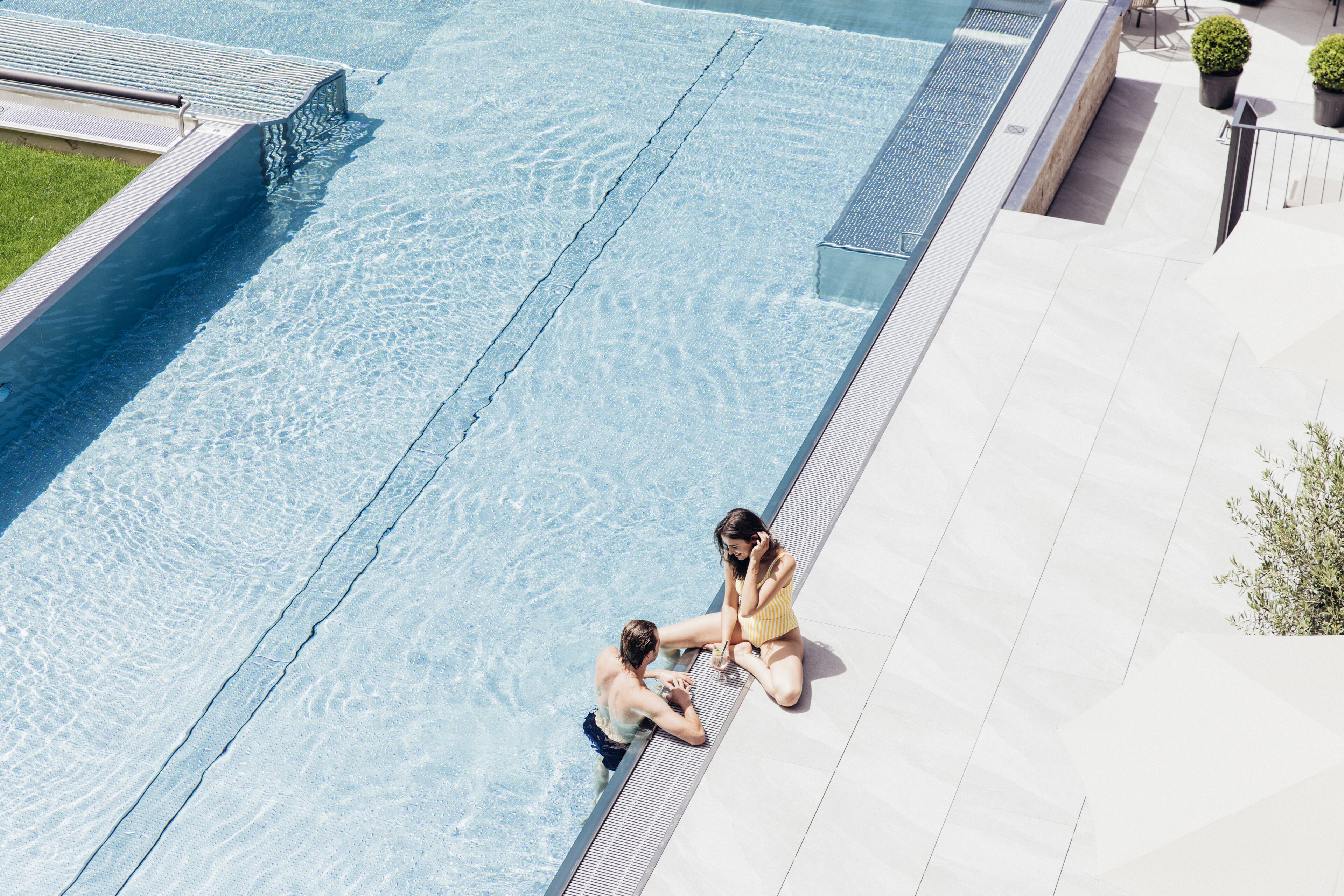 En swimmingpool med ett klart vatten, en kakelbeklädd poolterrass och en liten trädgårdsdel med krukväxter.