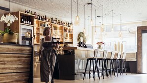 Una zona de bar con estantes de madera llenos de botellas, una barra y varios taburetes.