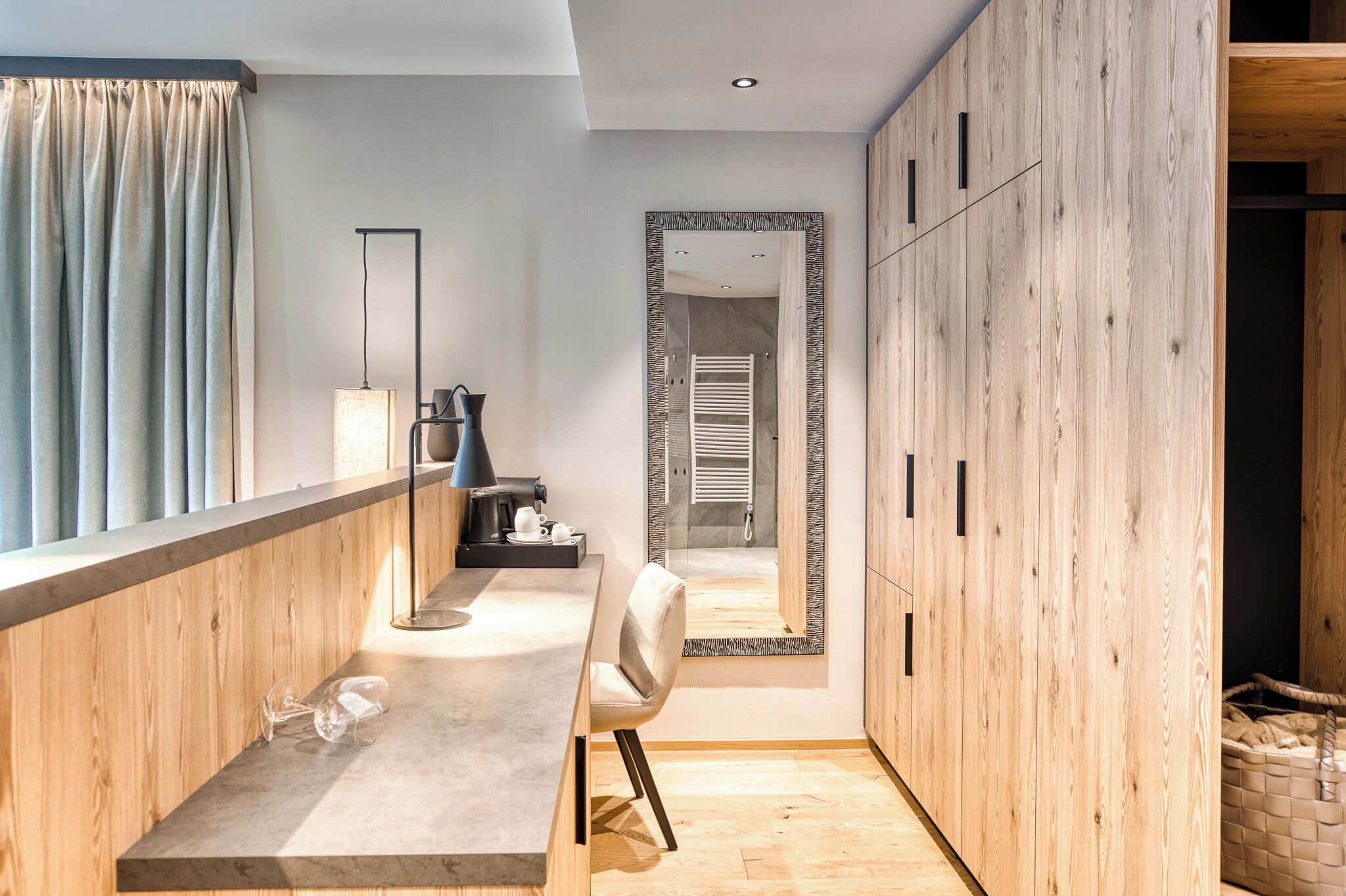 A modern interior with a wooden floor, a dining area with a table and chairs, a mirror, and a wardrobe.