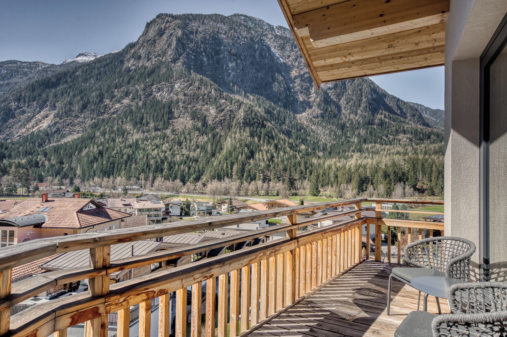 Ein Holzbalkon mit Blick auf ein Gebirge und eine Stadt darunter.