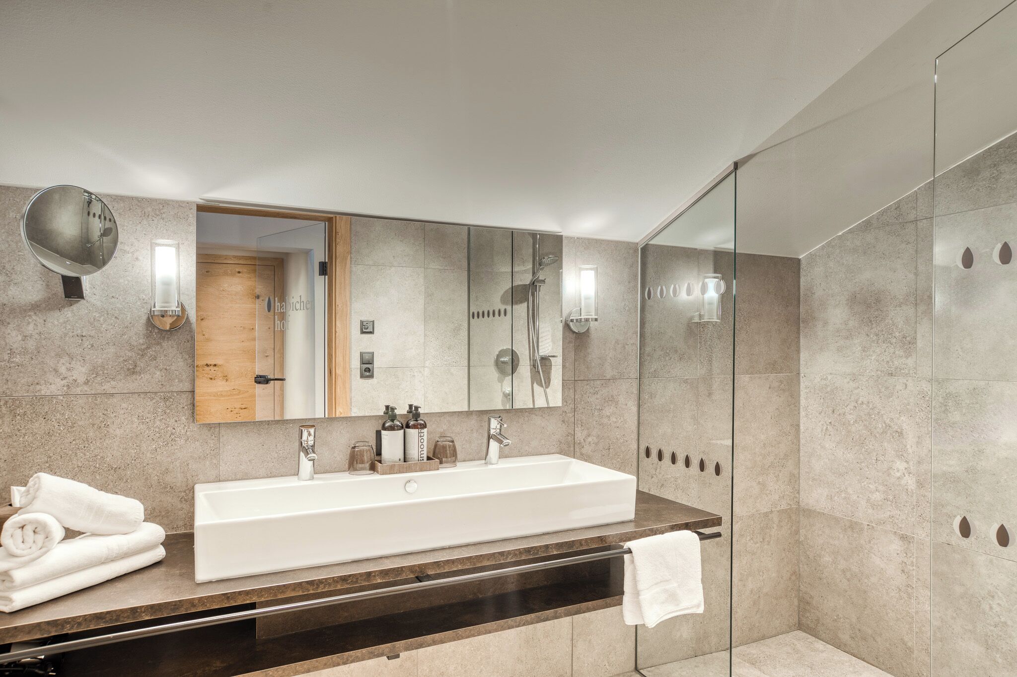 Un baño moderno con un espejo grande, un lavabo blanco y una cabina de ducha con paredes de vidrio.