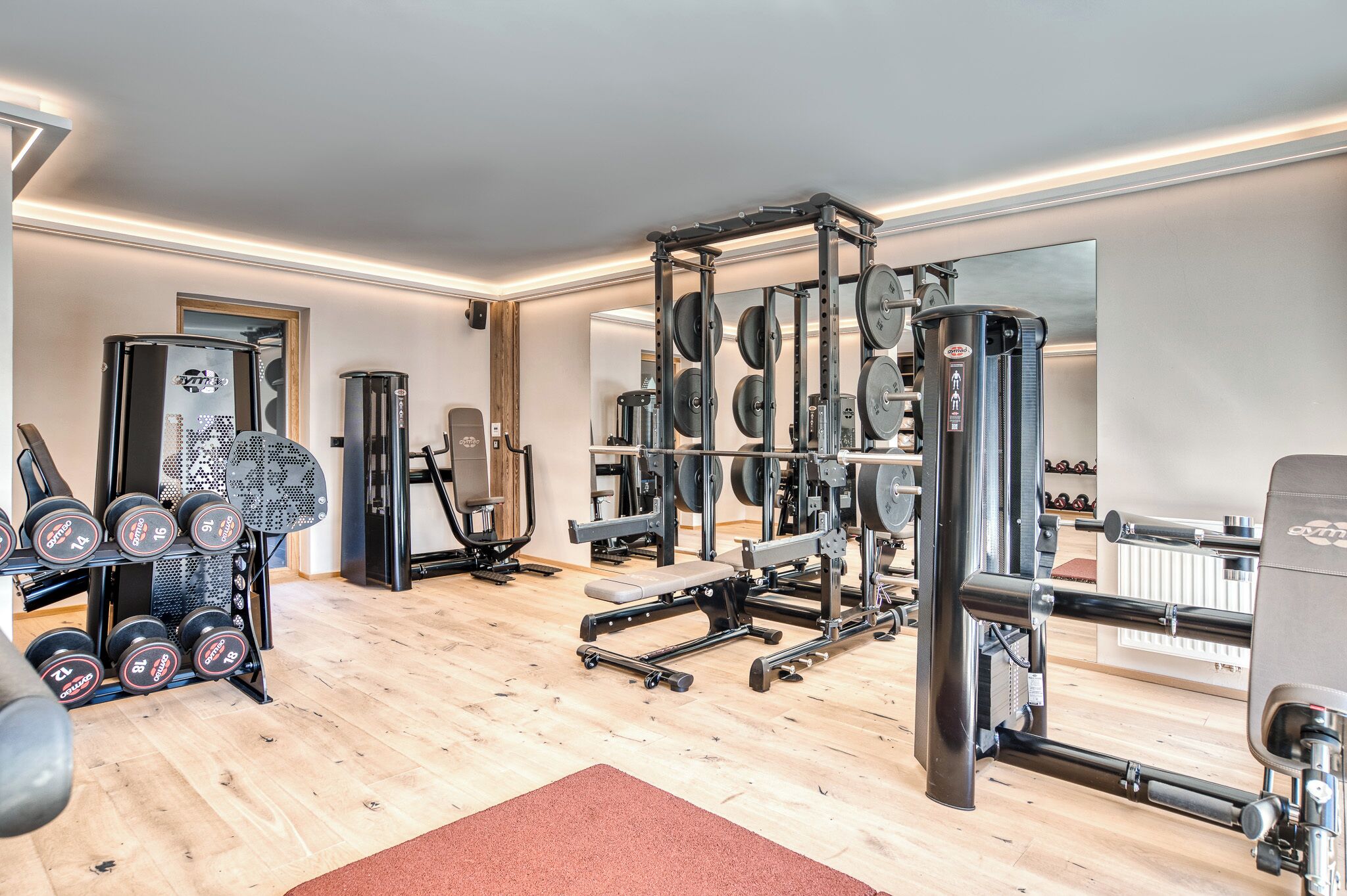 Un gimnasio con equipo de levantamiento de pesas, espejos y suelo de madera.
