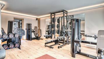 Un gimnasio con equipo de levantamiento de pesas, espejos y suelo de madera.