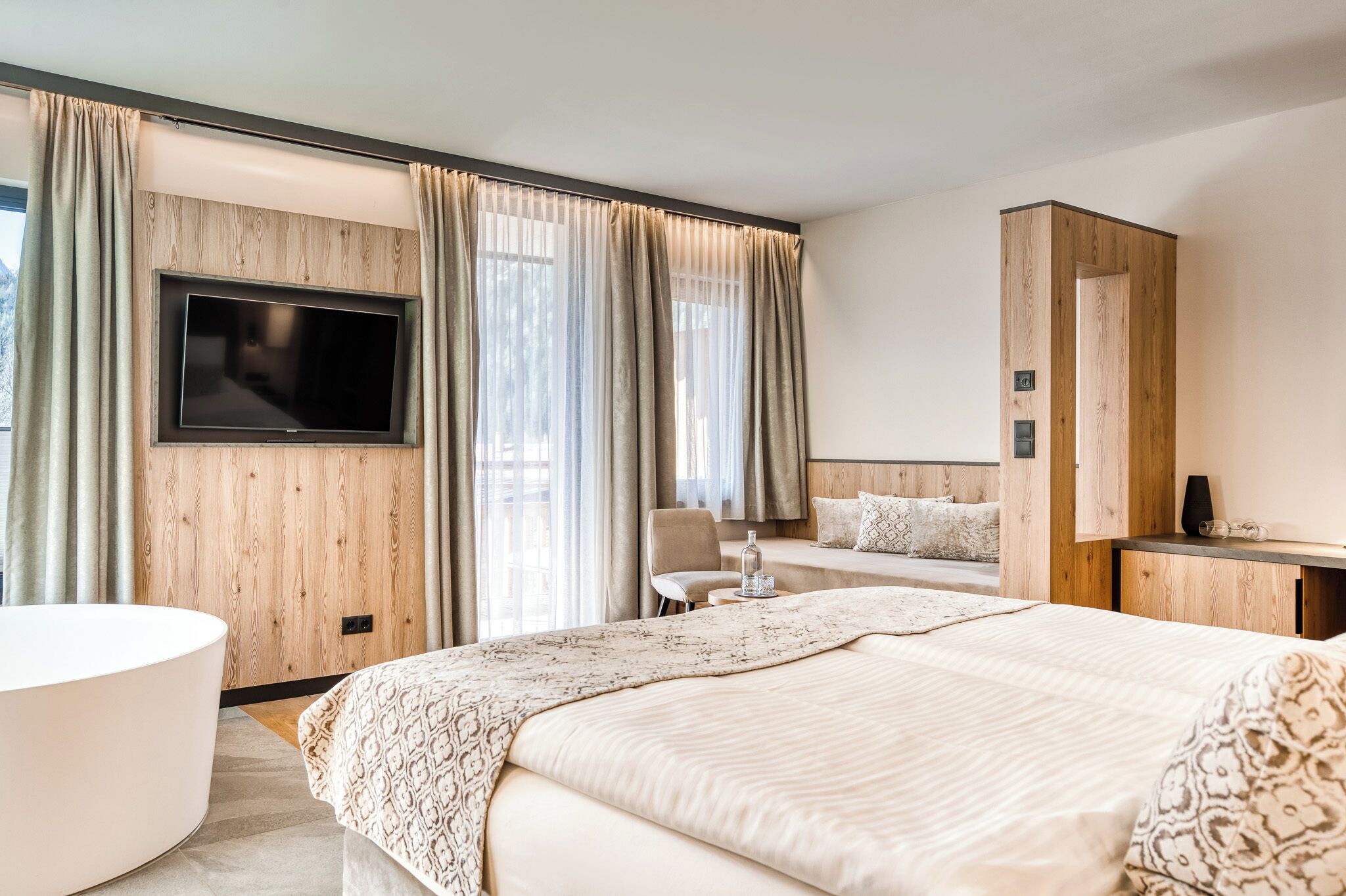 Ein modernes Hotelzimmer mit einem großen Bett, einem an der Wand befestigten Fernseher, einem Schreibtisch und einem Stuhl.