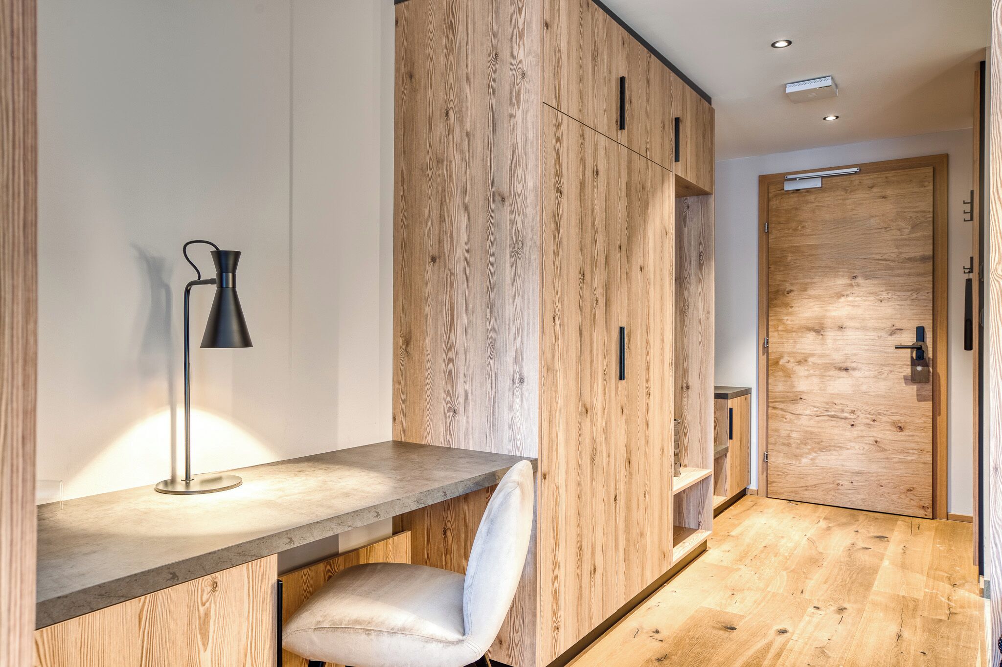 A modern room with a wooden wardrobe, a desk with a lamp, and a chair.