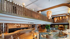 A spacious lobby with a wooden reception desk, seating areas, and a high ceiling with modern lighting fixtures.