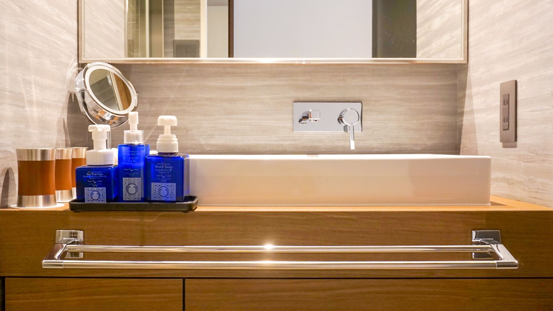 A modern bathroom with a large mirror, a sink, and toiletries on a tray.