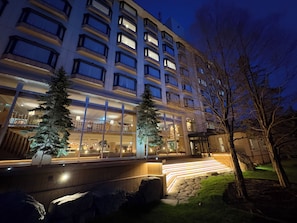 A multi-story hotel with a modern design, featuring a well-lit entrance and a landscaped outdoor area with trees and a stone pathway.
