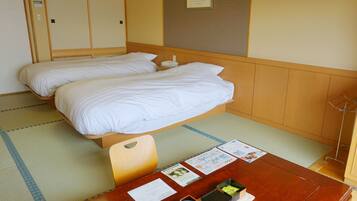 A hotel room with two beds, a wooden table with a bowl and papers, and a framed picture on the wall.