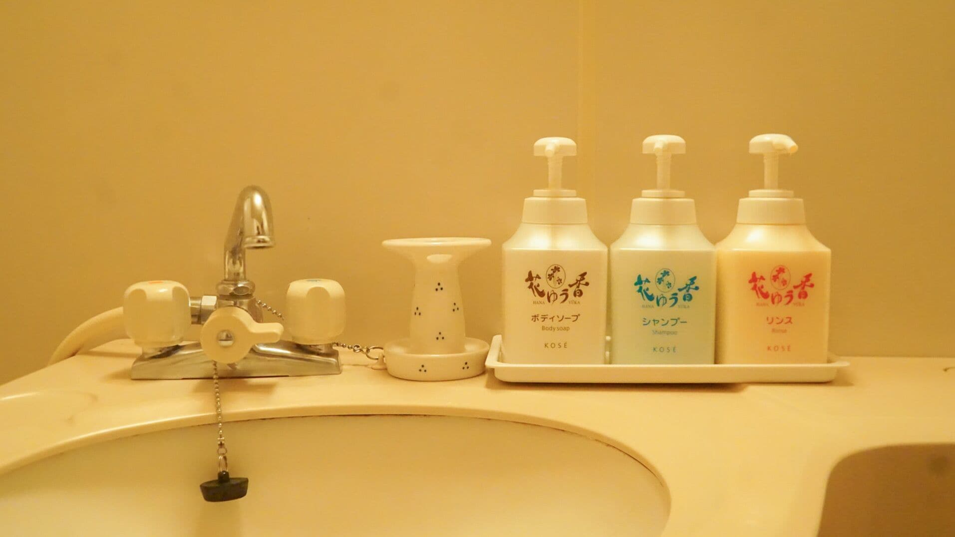A bathroom sink with a faucet, soap dispenser, and three bottles of shampoo.
