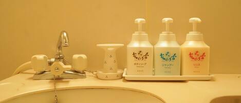 A bathroom sink with a faucet, soap dispenser, and three bottles of shampoo.