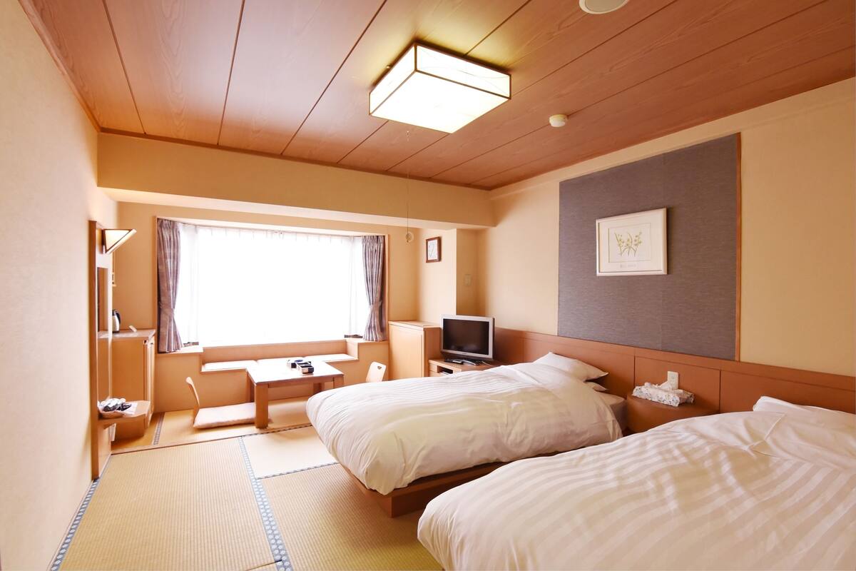 Une chambre d’hôtel avec deux lits, une télévision, un bureau et une fenêtre avec des rideaux.