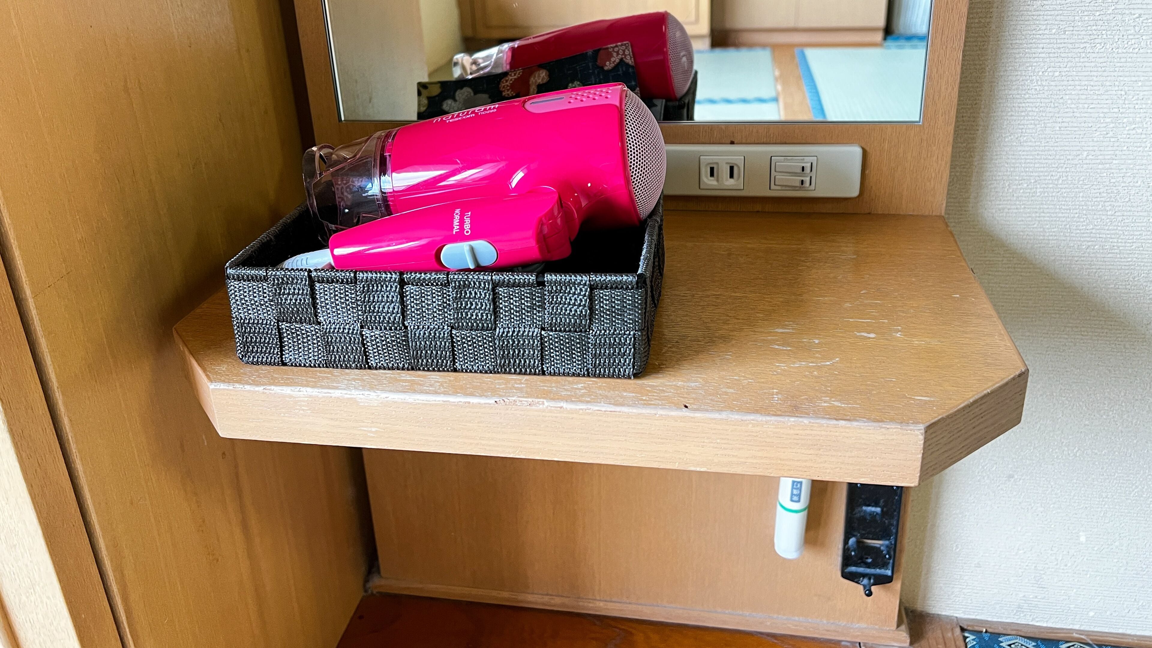 A storage box on a wooden shelf with a hairdryer inside.