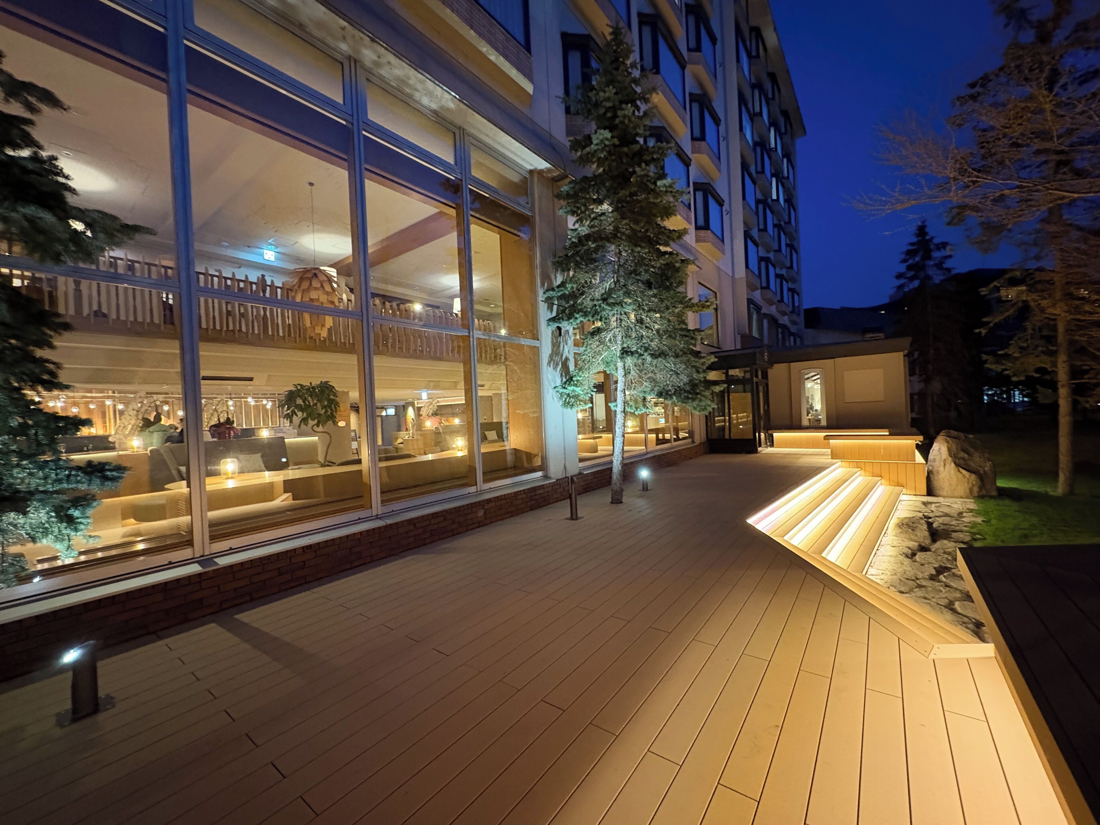 Een hotel met een glazen gevel, terras en een houten dek.