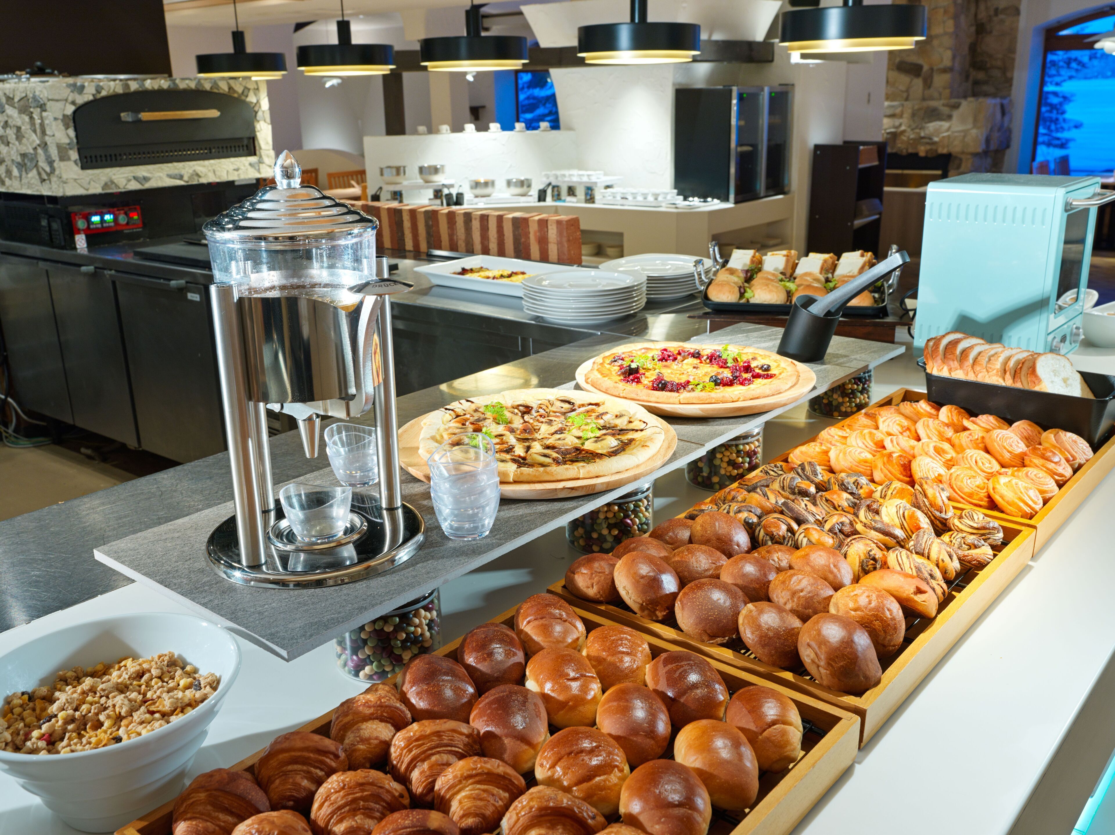 A buffet with various food items, including pizzas, pastries, and a coffee station.