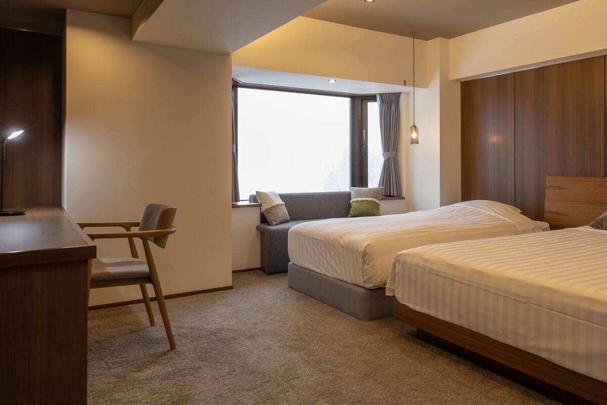 Une chambre d’hôtel équipée d’un bureau, de deux lits, d’une fenêtre avec des rideaux et offrant une vue sur le ciel.